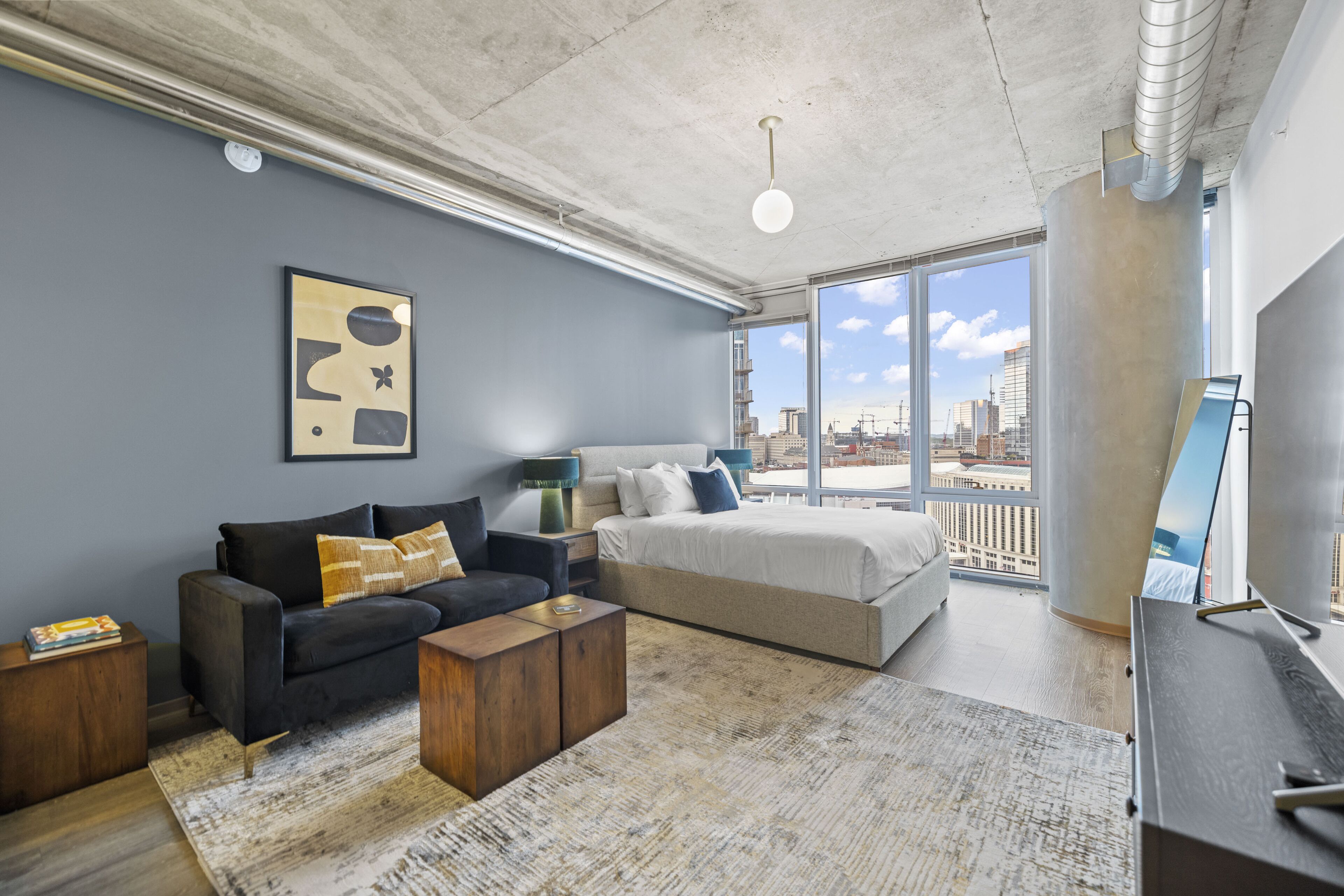 Un dormitorio moderno con una cama grande, un sofá y vistas de la ciudad a través de amplios ventanales.