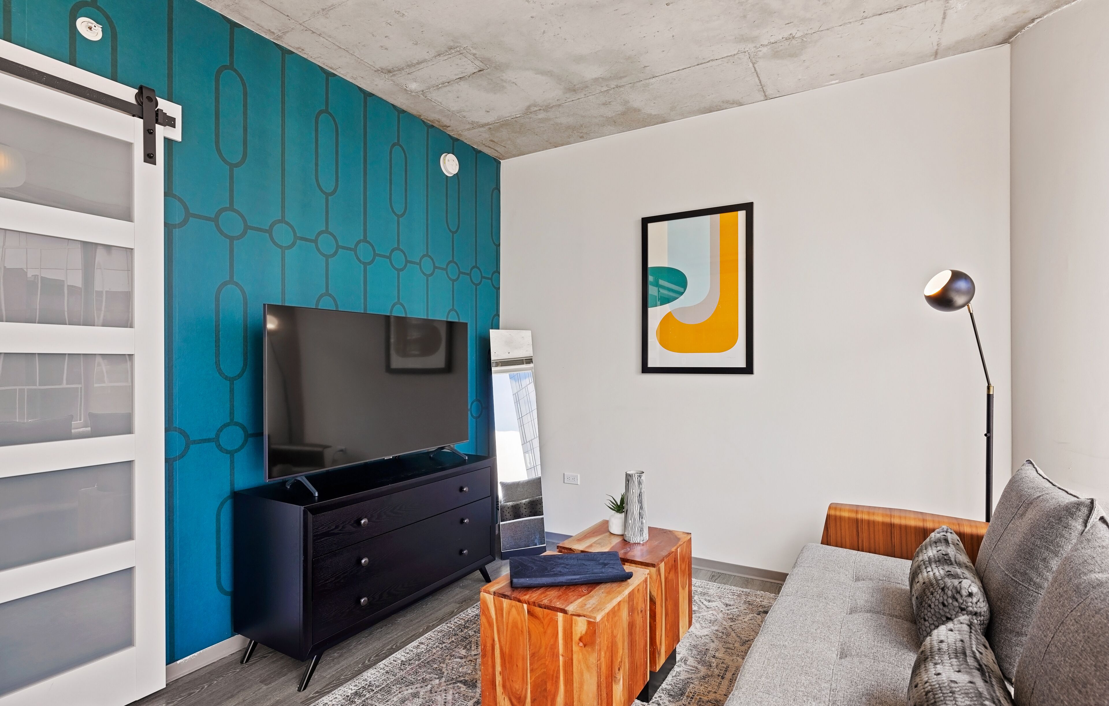 A modern living room with a large flat-screen TV, a wooden coffee table, a sofa, and a blue accent wall.