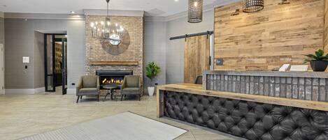 A modern lobby with a fireplace, seating area, and a reception desk with a wooden counter and black cushioned backrest.