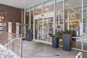Placemakr Premier's sleek entrance features glass doors, metal railings, and lush greenery.