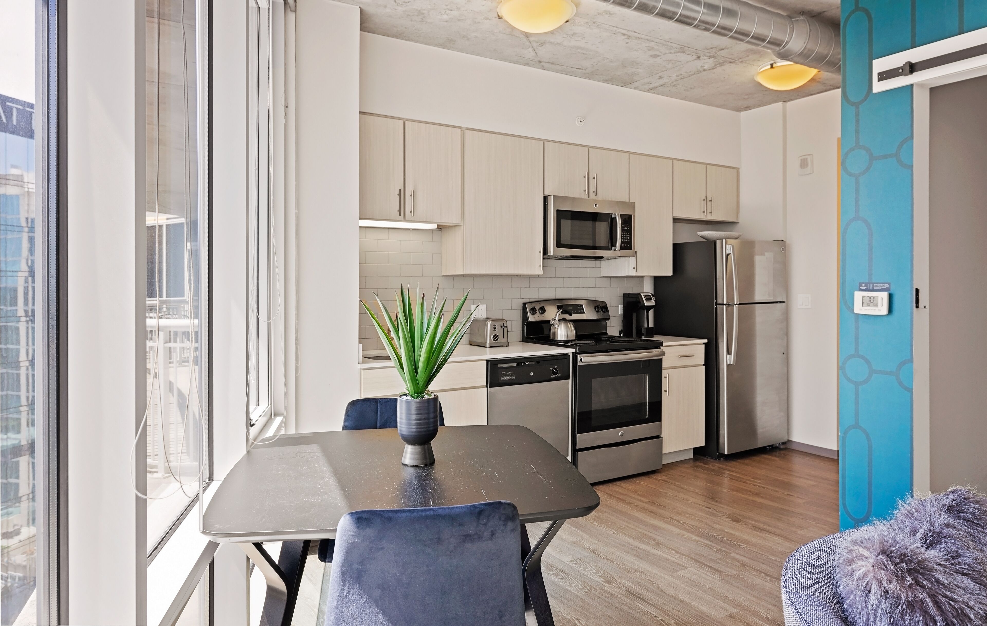A modern kitchen with stainless steel appliances, a dining area with a table and chairs, and a view of the city through large windows.