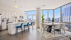 Cocina moderna con una isla central, comedor con mesa y sillas, y ventanas amplias con vistas a la ciudad.