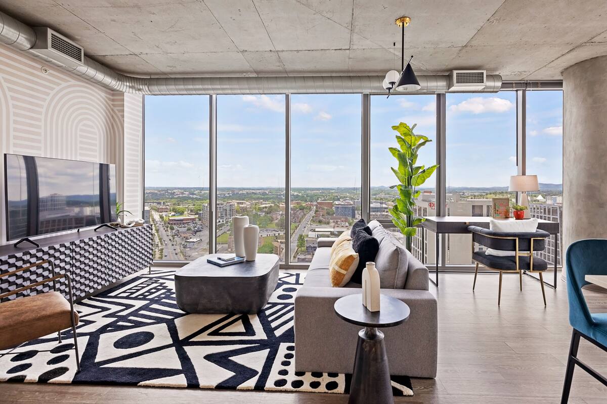 A modern living room with a large TV, a sofa, a coffee table, and a view of the city.
