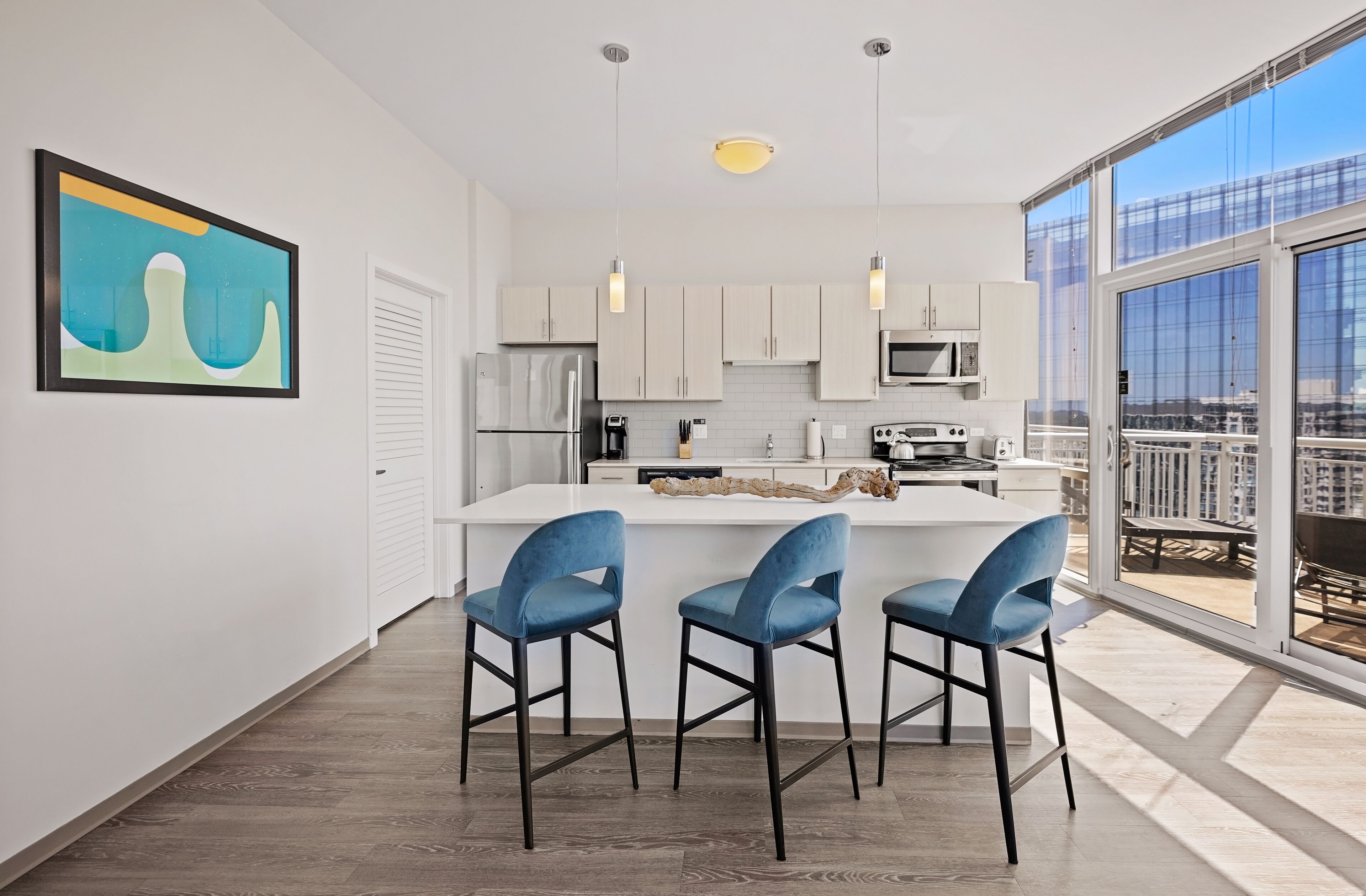 A modern kitchen with a central island, bar stools, and a large window offering a city view.