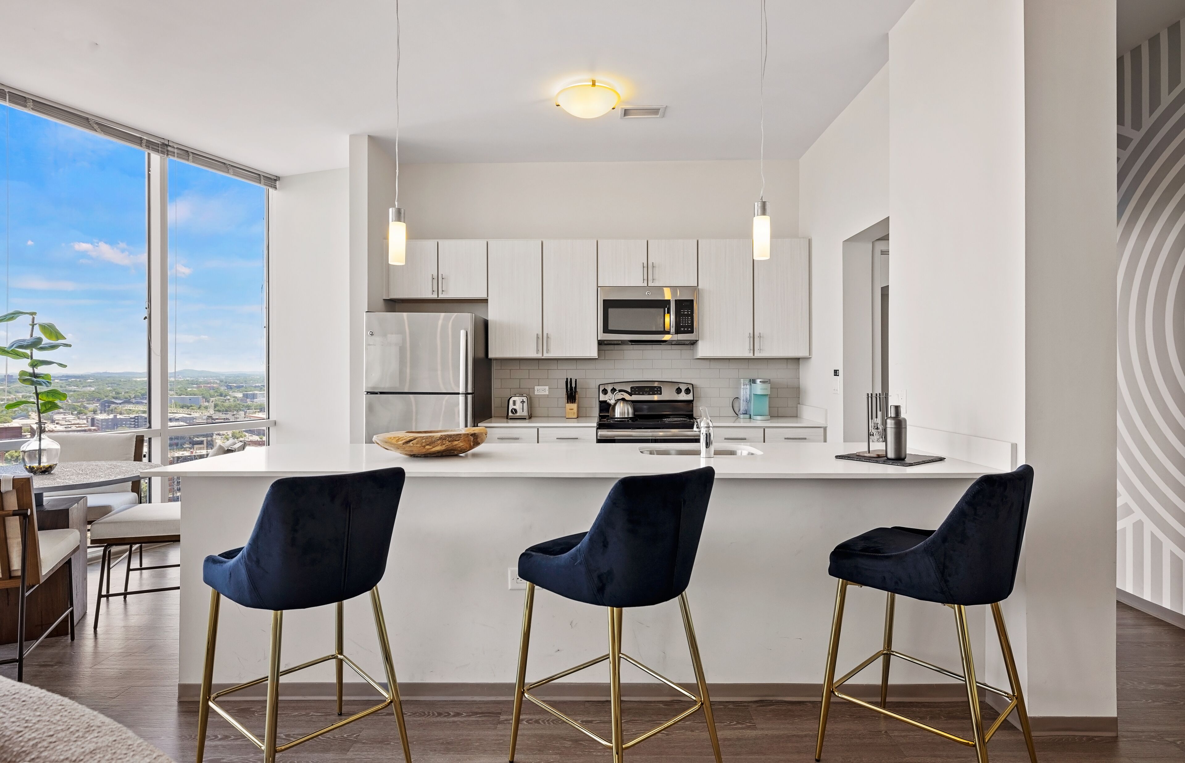 A modern kitchen with white cabinets, a stainless steel microwave, and a large island with bar stools.