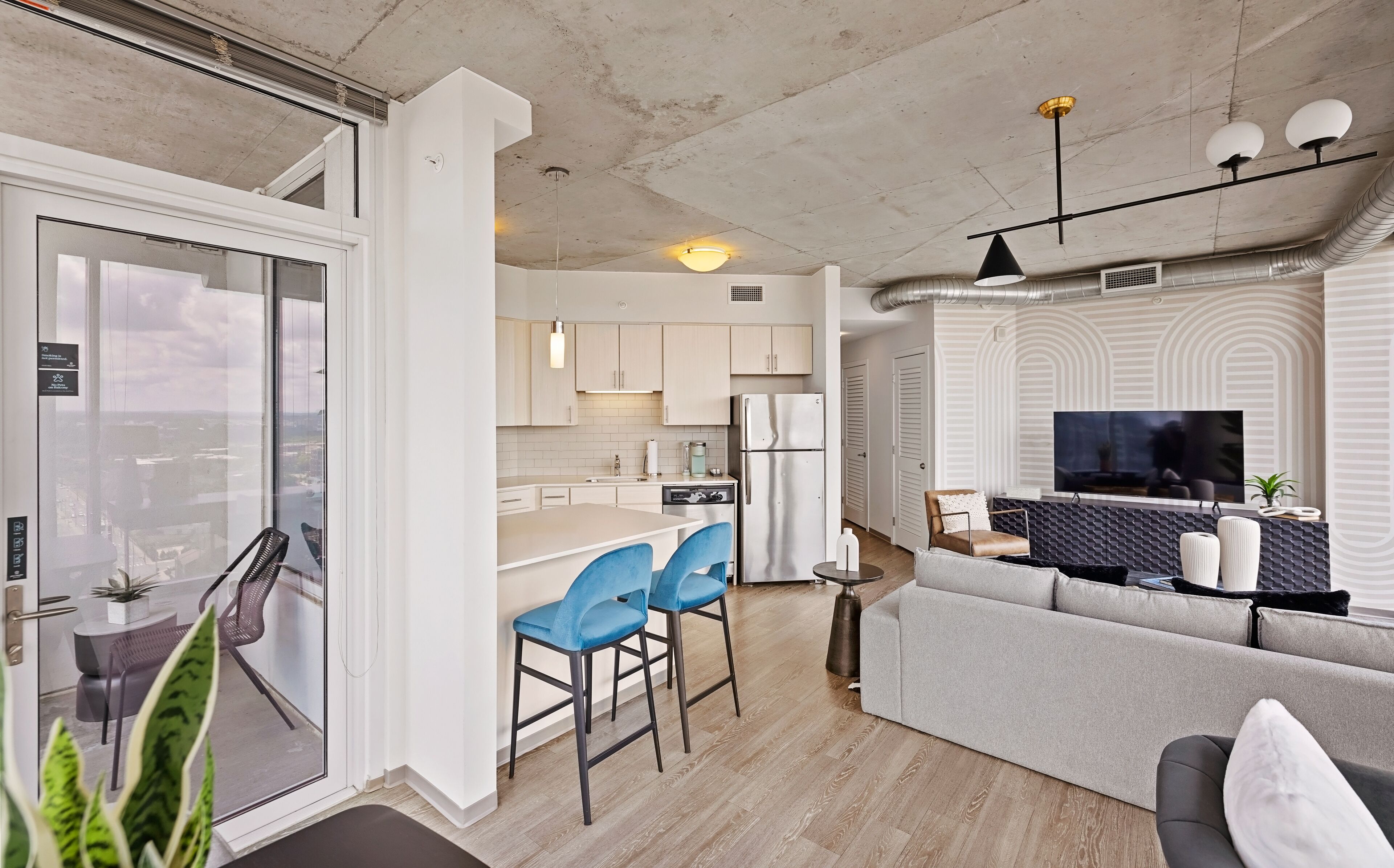 A modern apartment with a kitchen, dining area, and living room. It features a large window, a flat-screen TV, and a sofa.