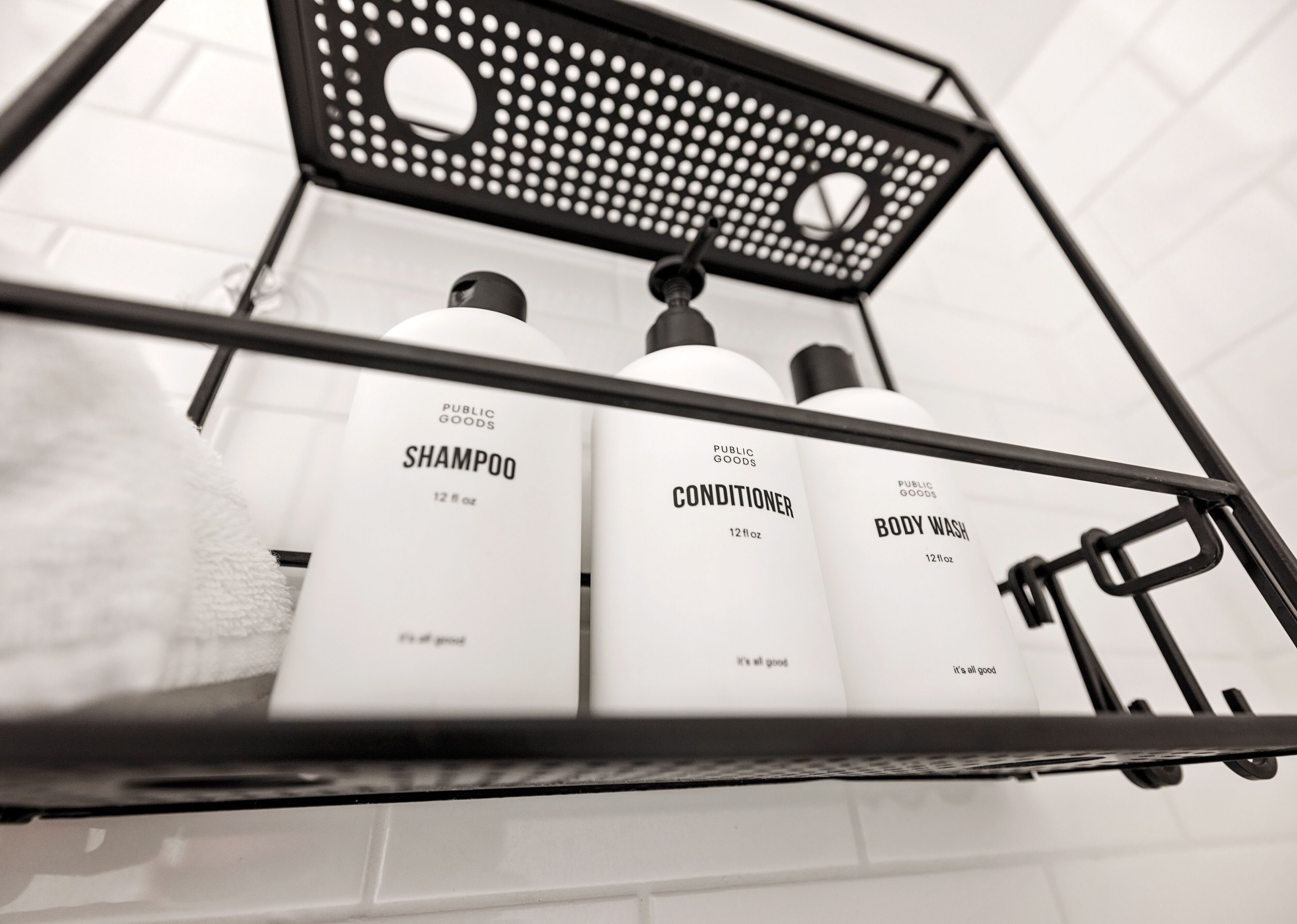 A bathroom shelf with three toiletry bottles labeled 'Shampoo', 'Conditioner', and 'Body Wash'.