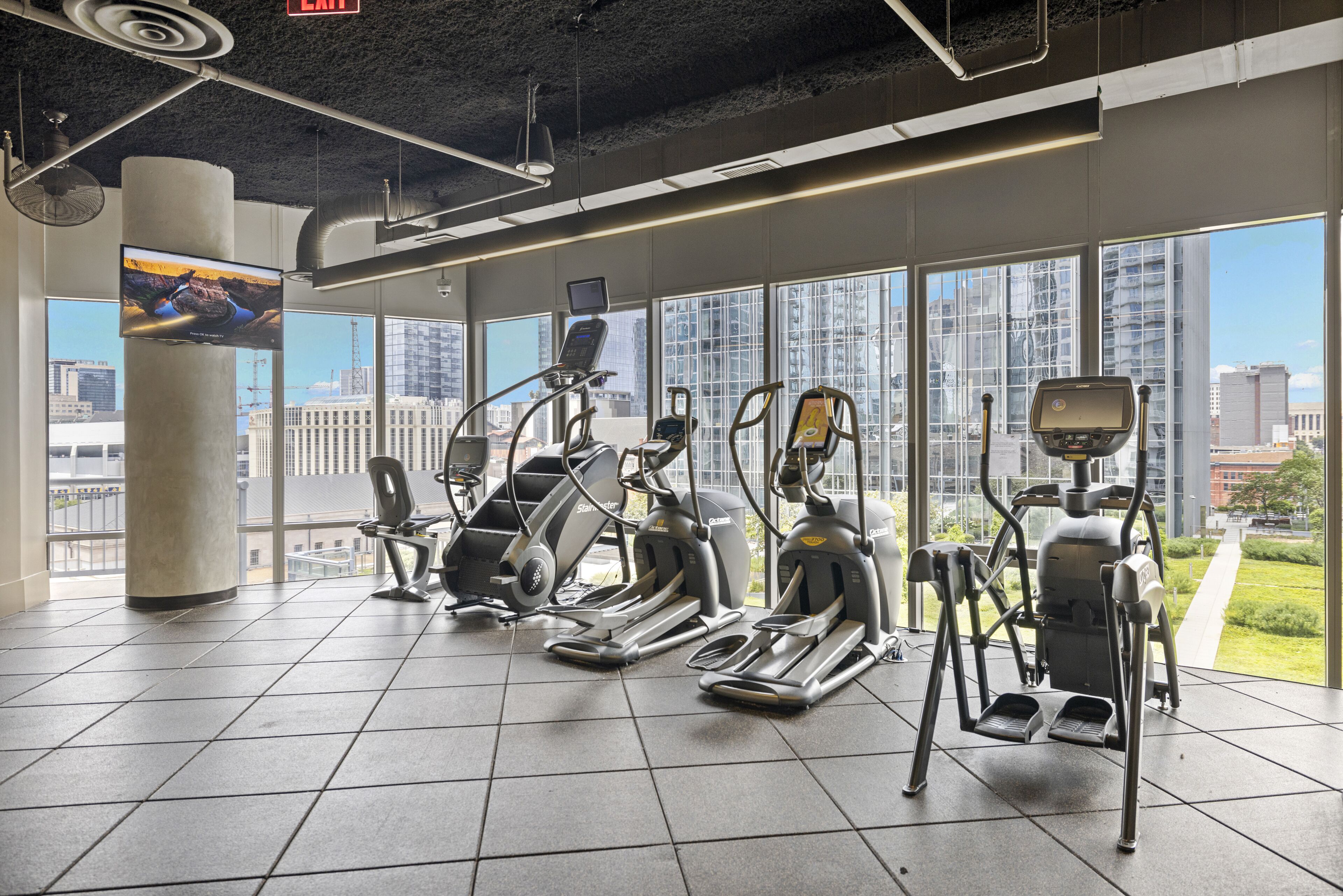 A gym with various exercise machines, large windows, and a city view.