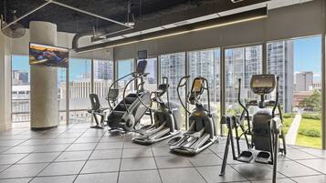 A gym with various exercise machines, large windows, and a city view.