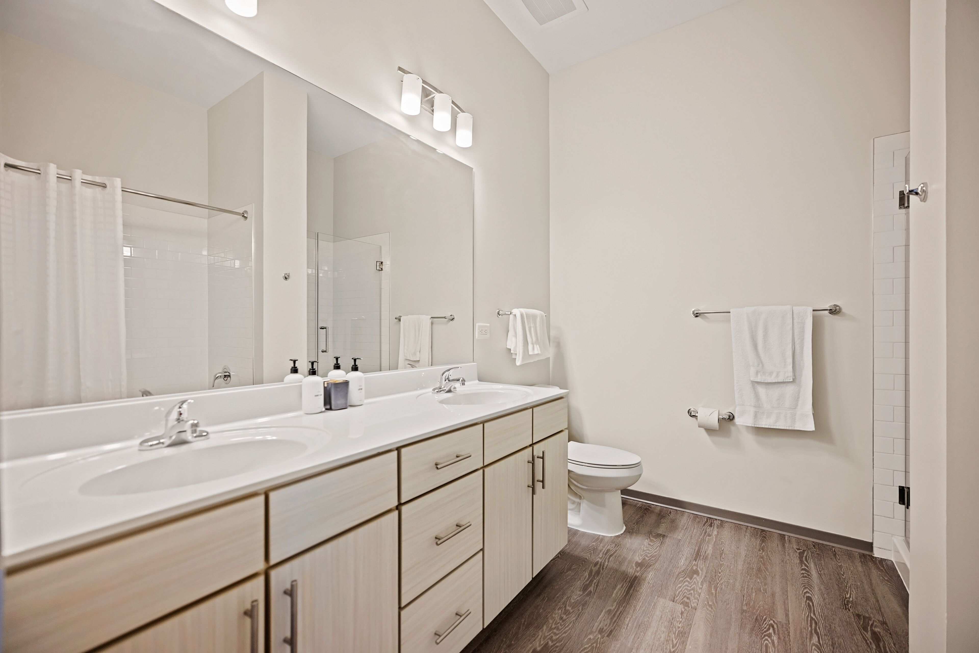 Un baño moderno con un espejo grande, dos lavamanos, un inodoro y una ducha.