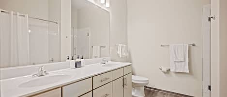 Un baño moderno con un espejo grande, dos lavamanos, un inodoro y una ducha.