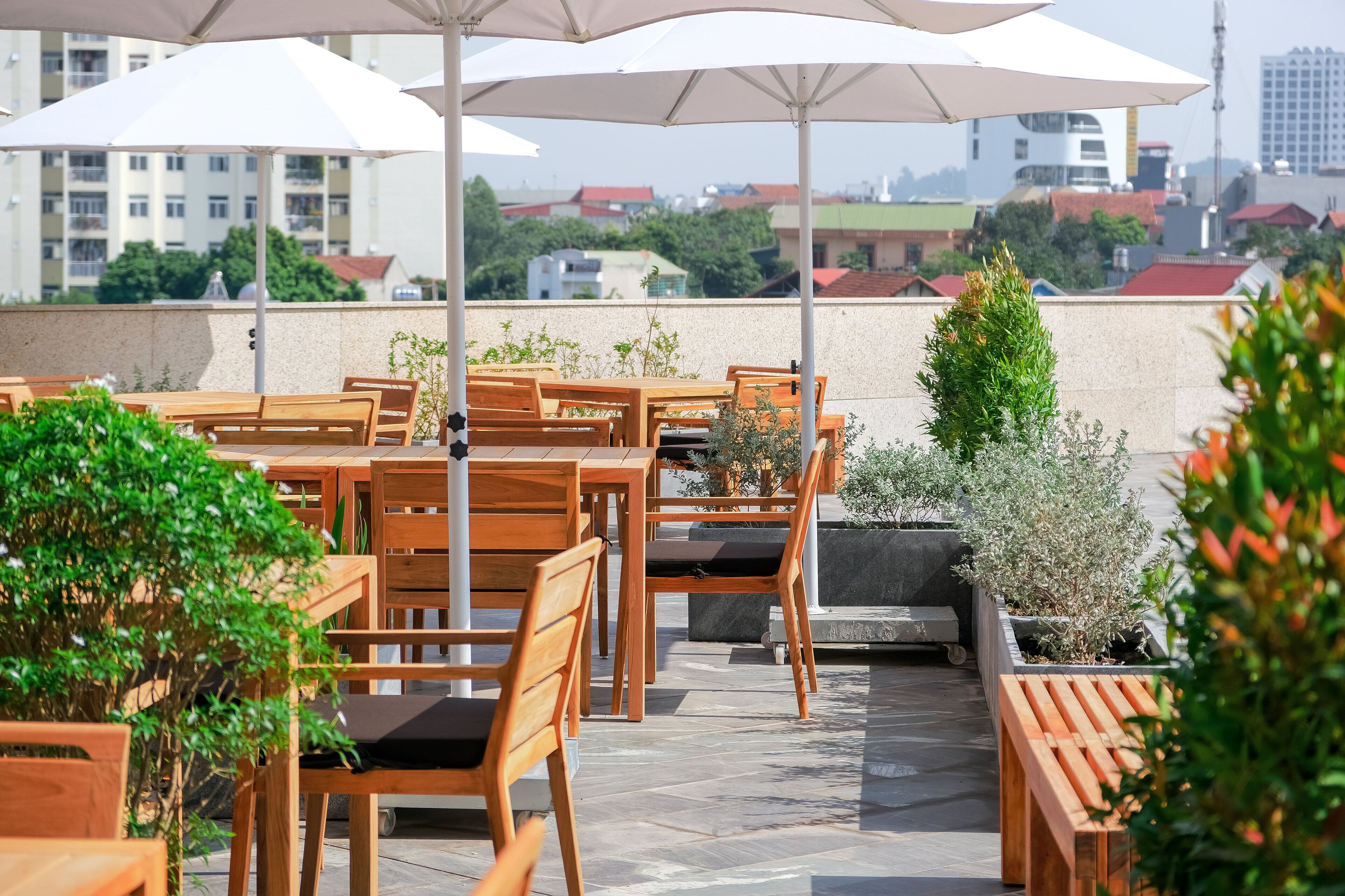 An outdoor seating area with wooden tables and chairs, large umbrellas, and potted plants.