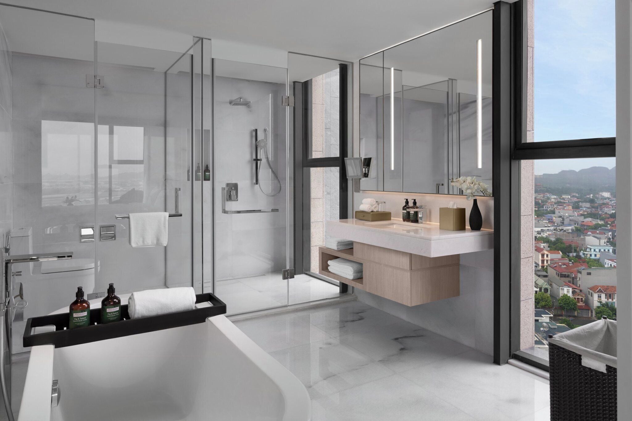 Un baño moderno con ducha envuelta en cristal, una bañera grande e un tocador con vistas a la ciudad.