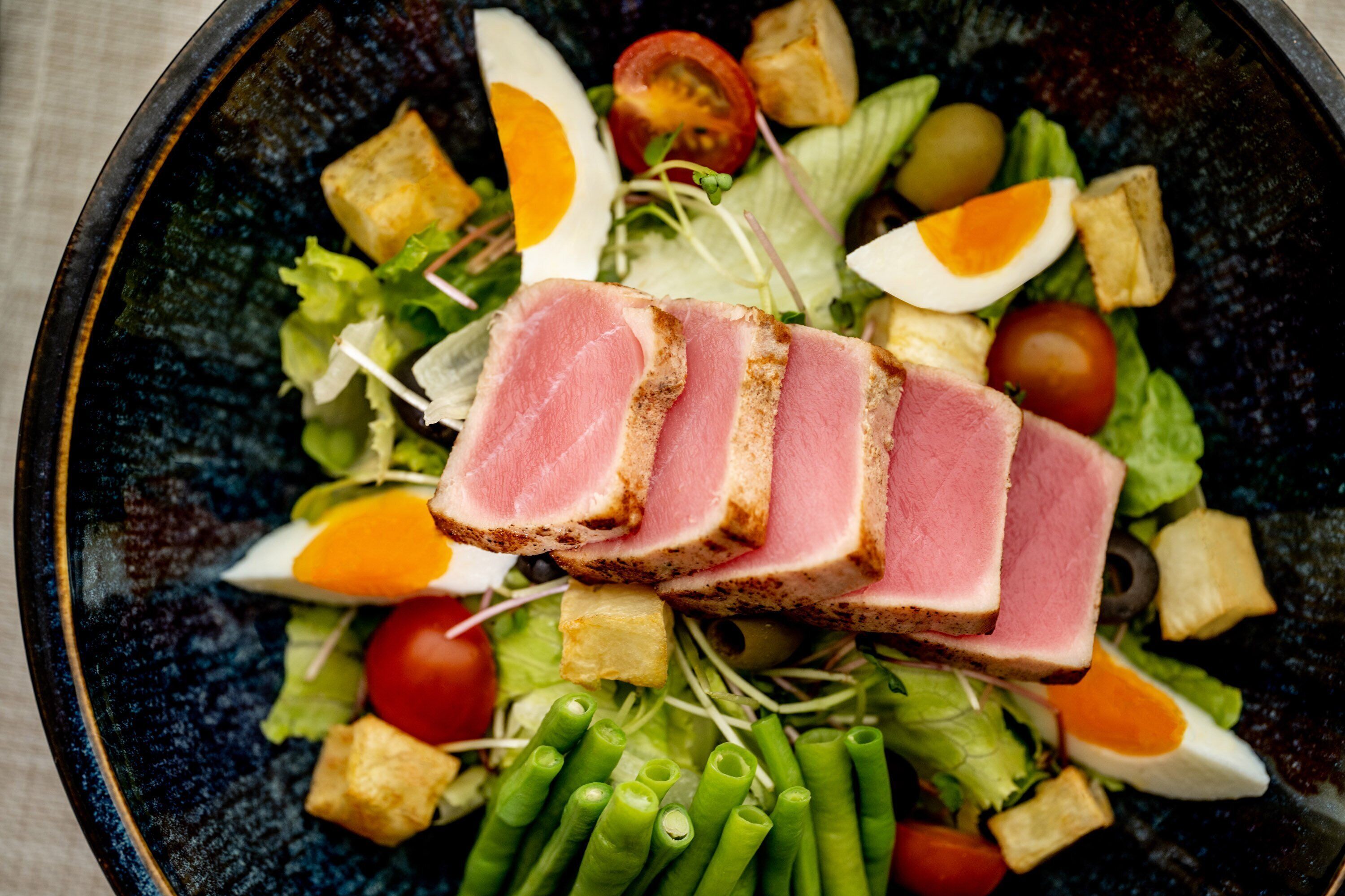 A salad with various vegetables and a slice of meat.