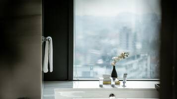 A bathroom with a large window, a white sink, a vase with flowers, and a towel rack.