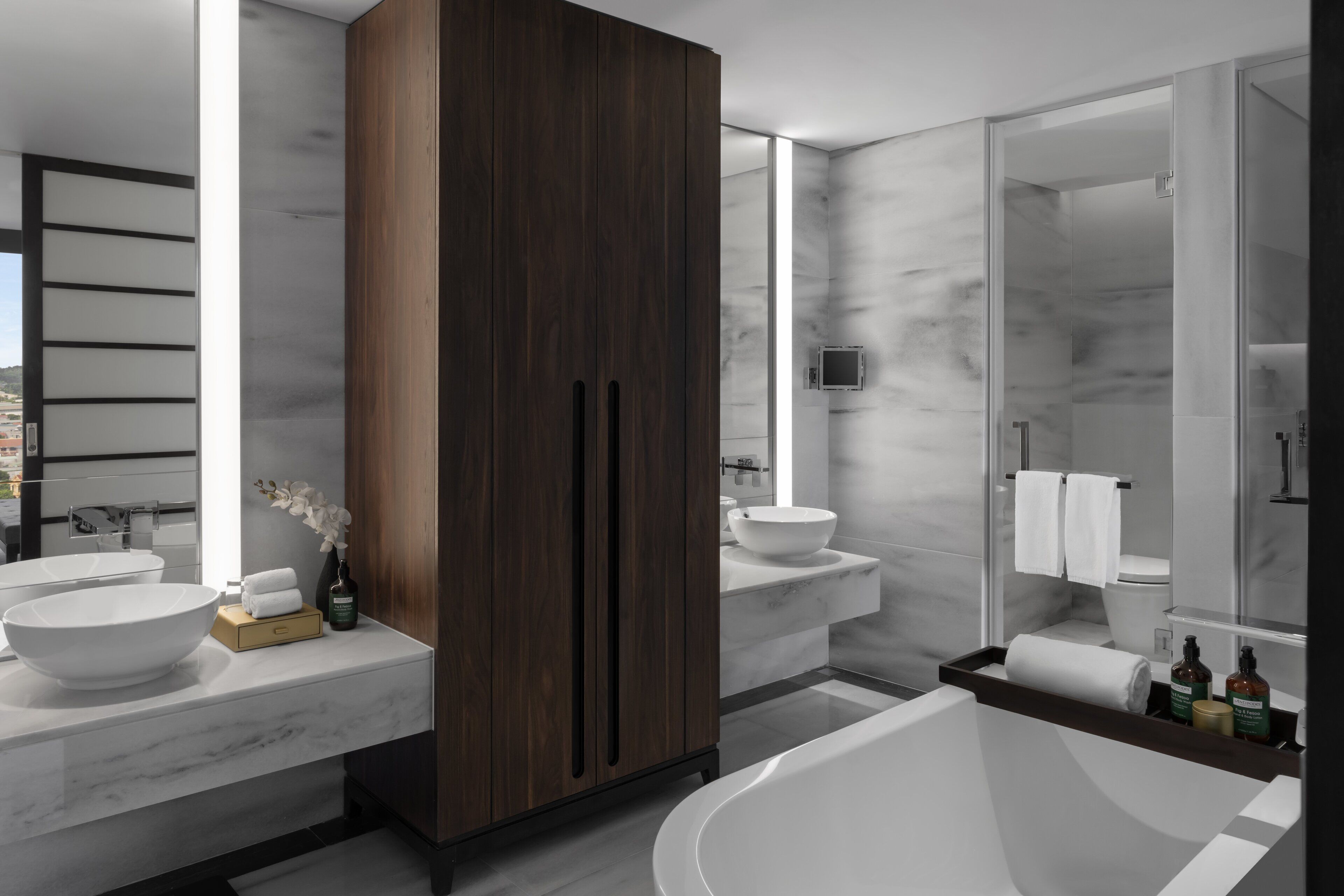 A modern bathroom with a large bathtub, two sinks, and a wooden wardrobe.