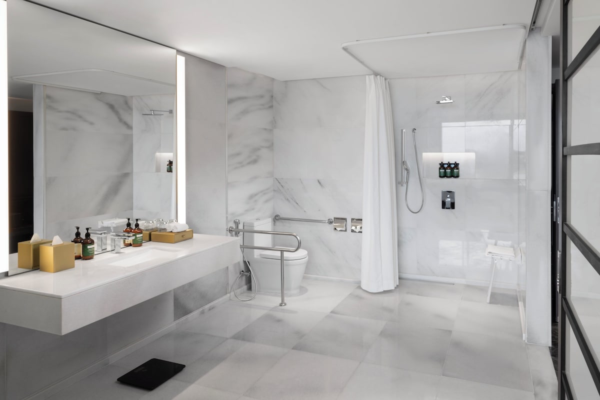A modern bathroom with a large mirror, a vanity with toiletries, a shower area, and a toilet.