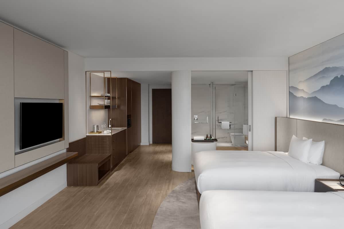 A modern hotel room with a TV, a large bed, a sofa, a bathroom, and a painting on the wall.