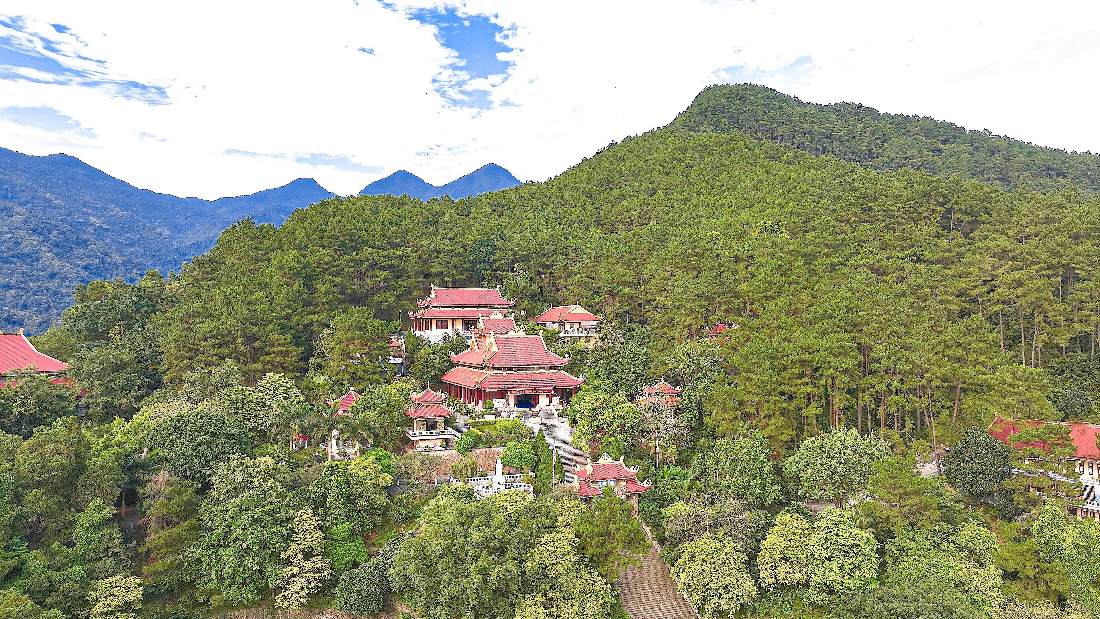 A traditional multi-tiered temple complex surrounded by dense forest and mountains.