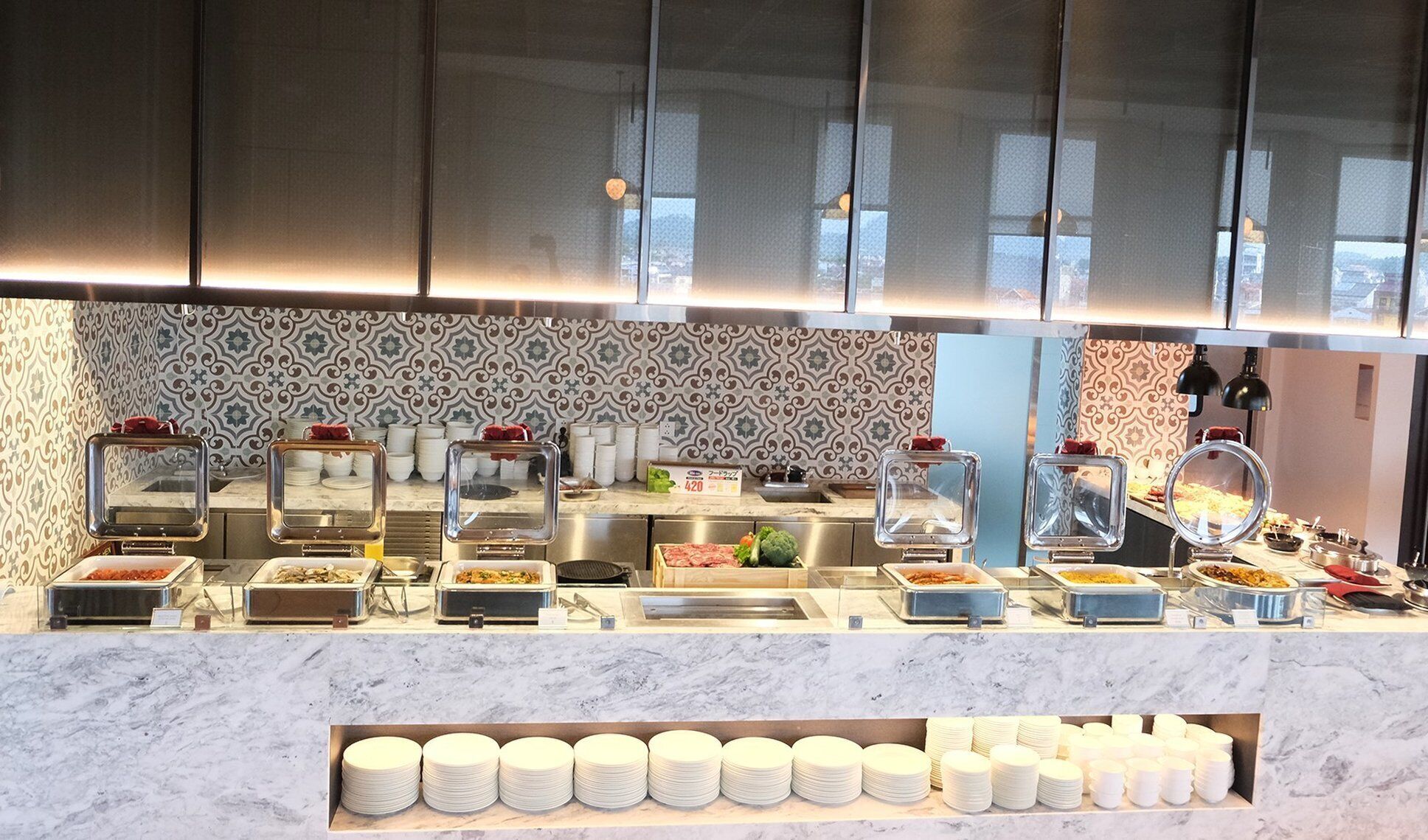 Montaje tipo buffet con varias estaciones de comida, incluyendo una sección de carnes y una barra de ensaladas, con un salpicadero de azulejos y una encimera de mármol.