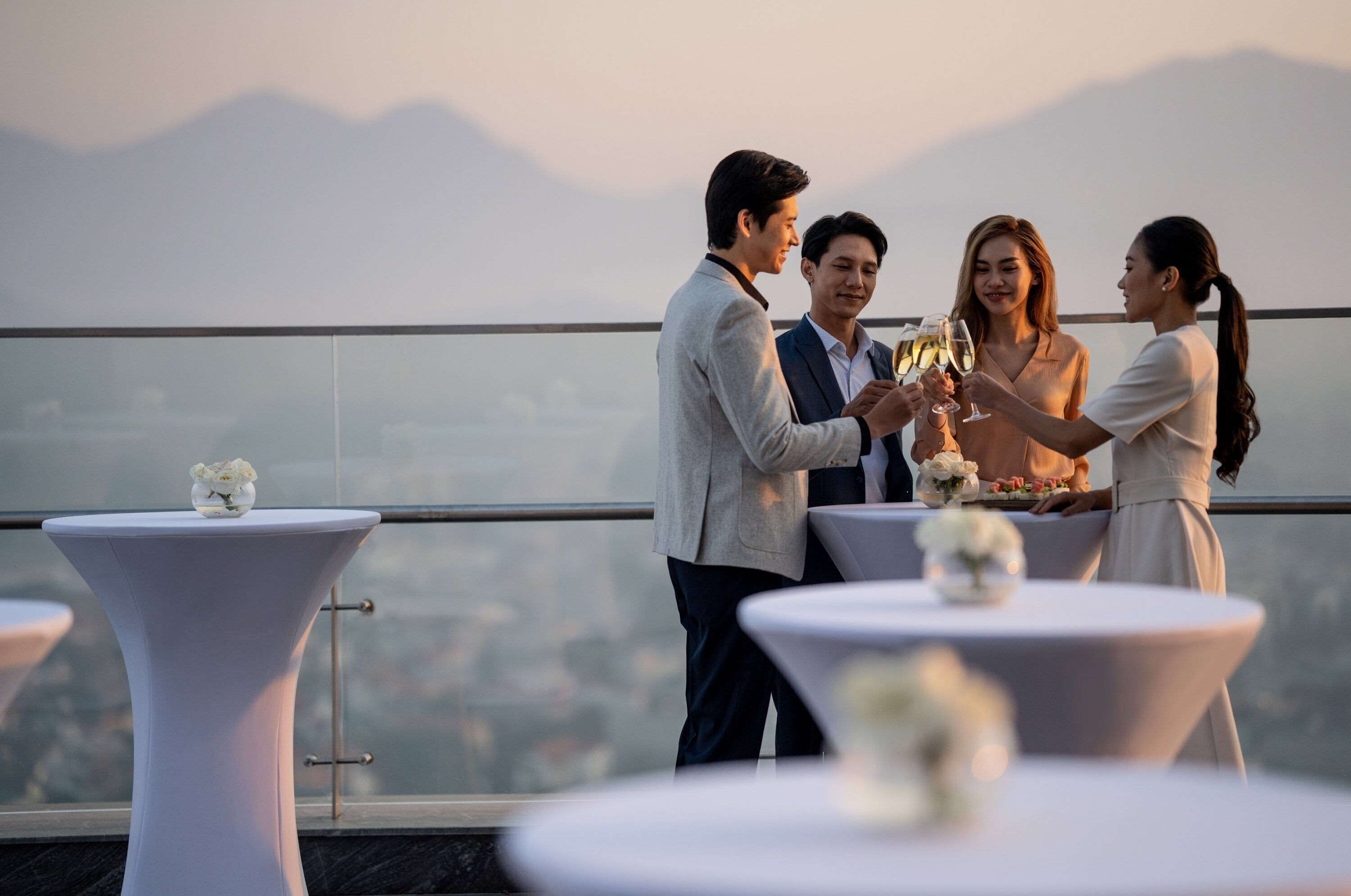 A rooftop terrace with round tables, each with a white vase of flowers.