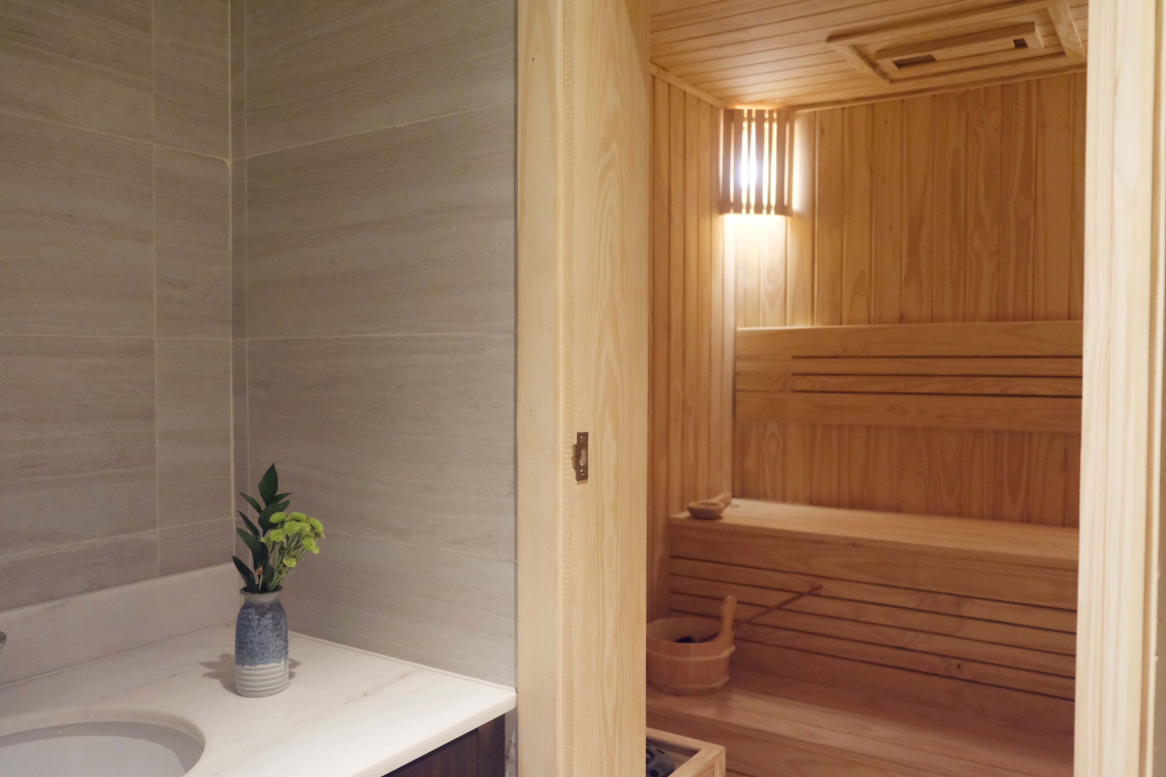 Una sauna in legno con una panca, una piccola pianta su un ripiano e un lampadario sopra la panca.