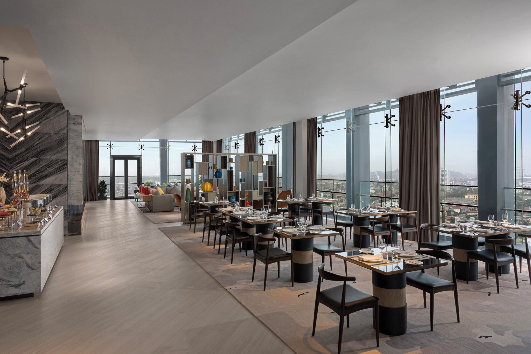 A modern dining area with multiple tables and chairs, large windows offering a city view, and a marble wall with a unique design.