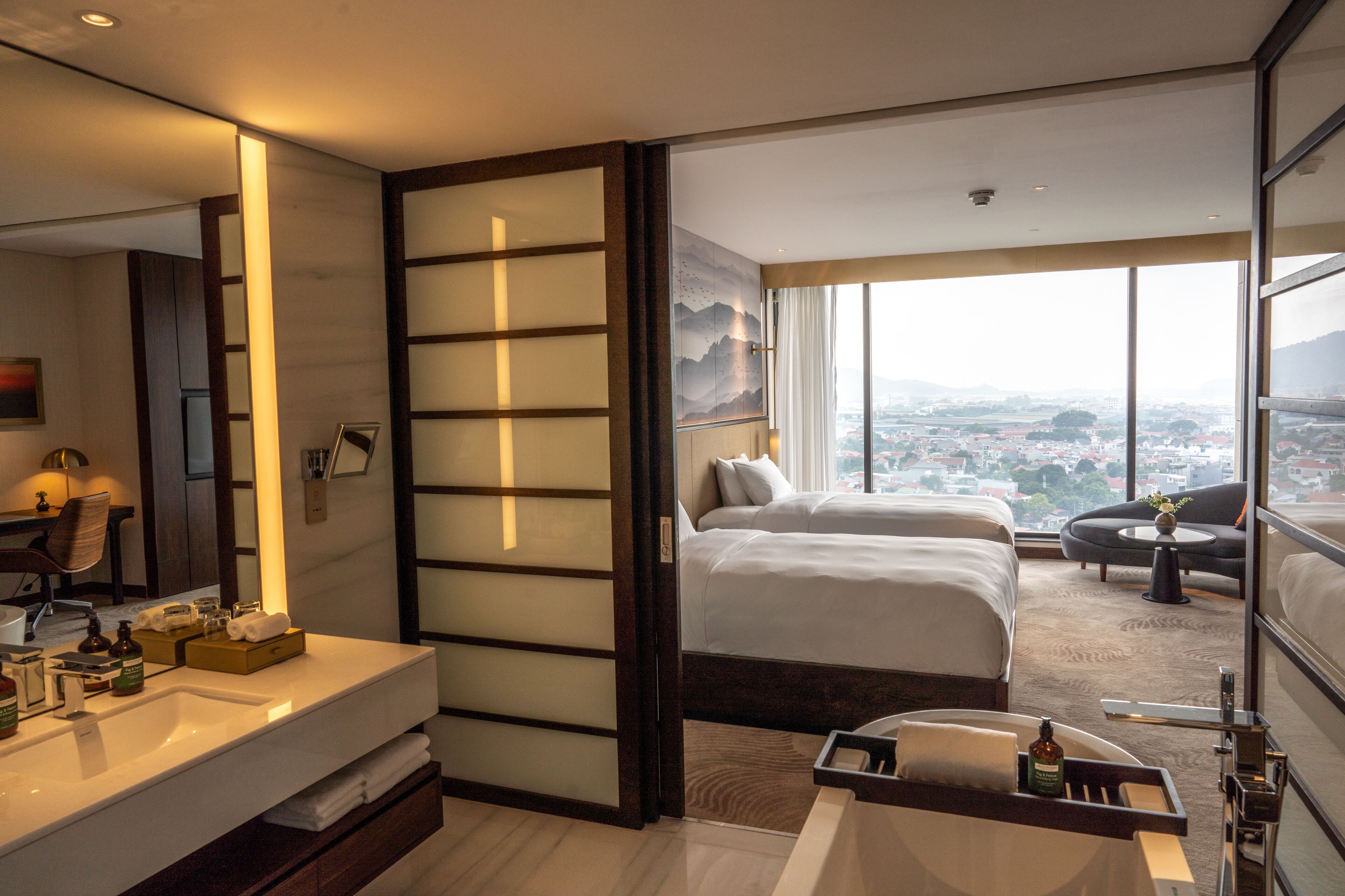 A hotel room with a large bed, a sofa, a desk, and a view of the city.