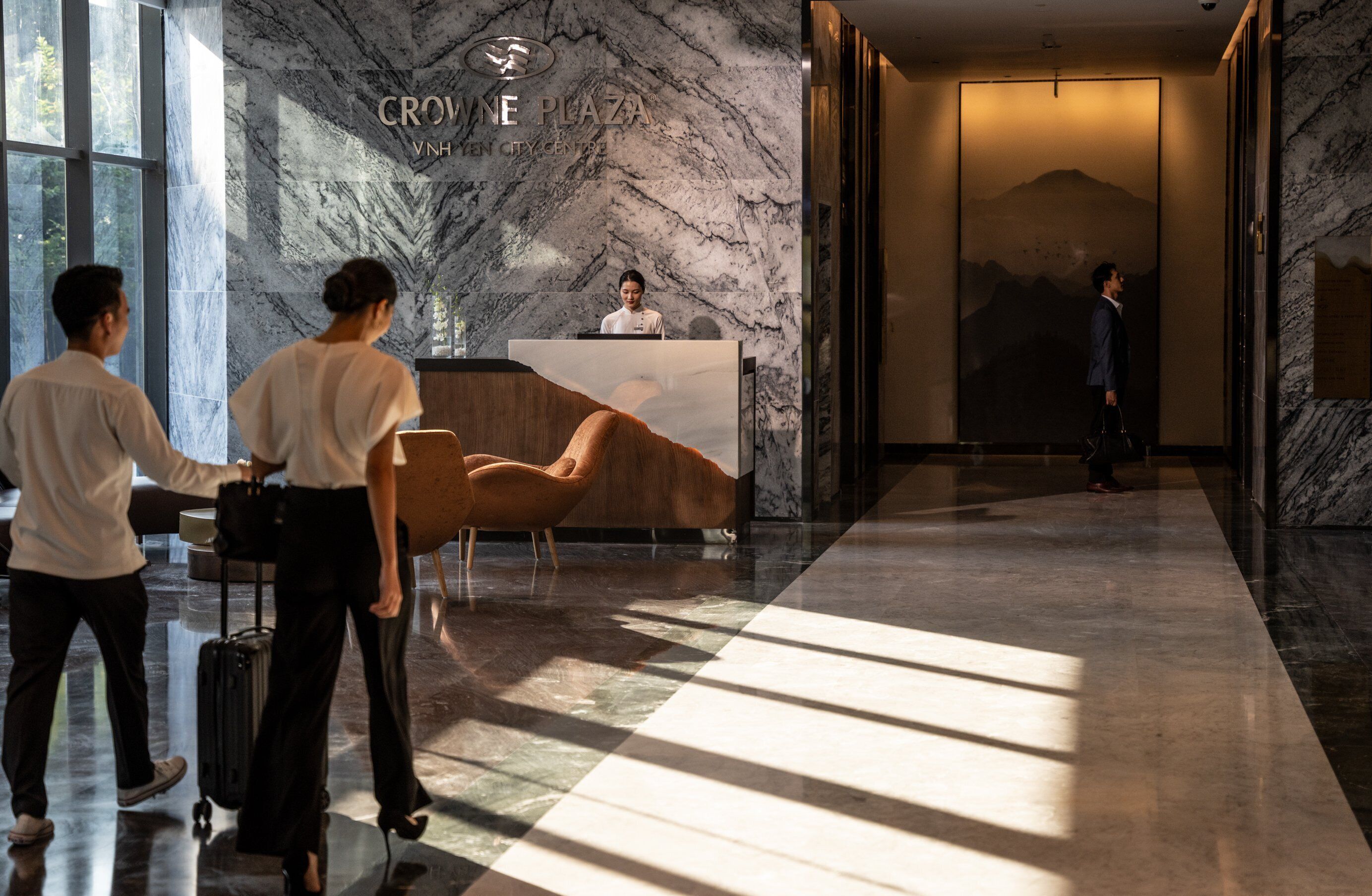 A hotel lobby with a reception desk, a large mural, and a modern design.