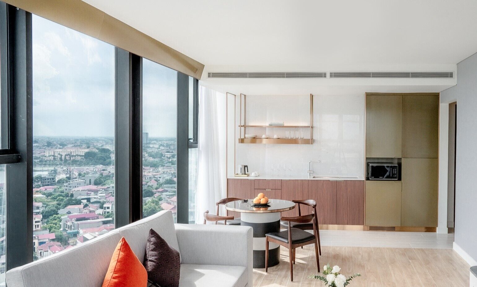 A modern apartment with a dining area, kitchen, and a large window offering a city view.
