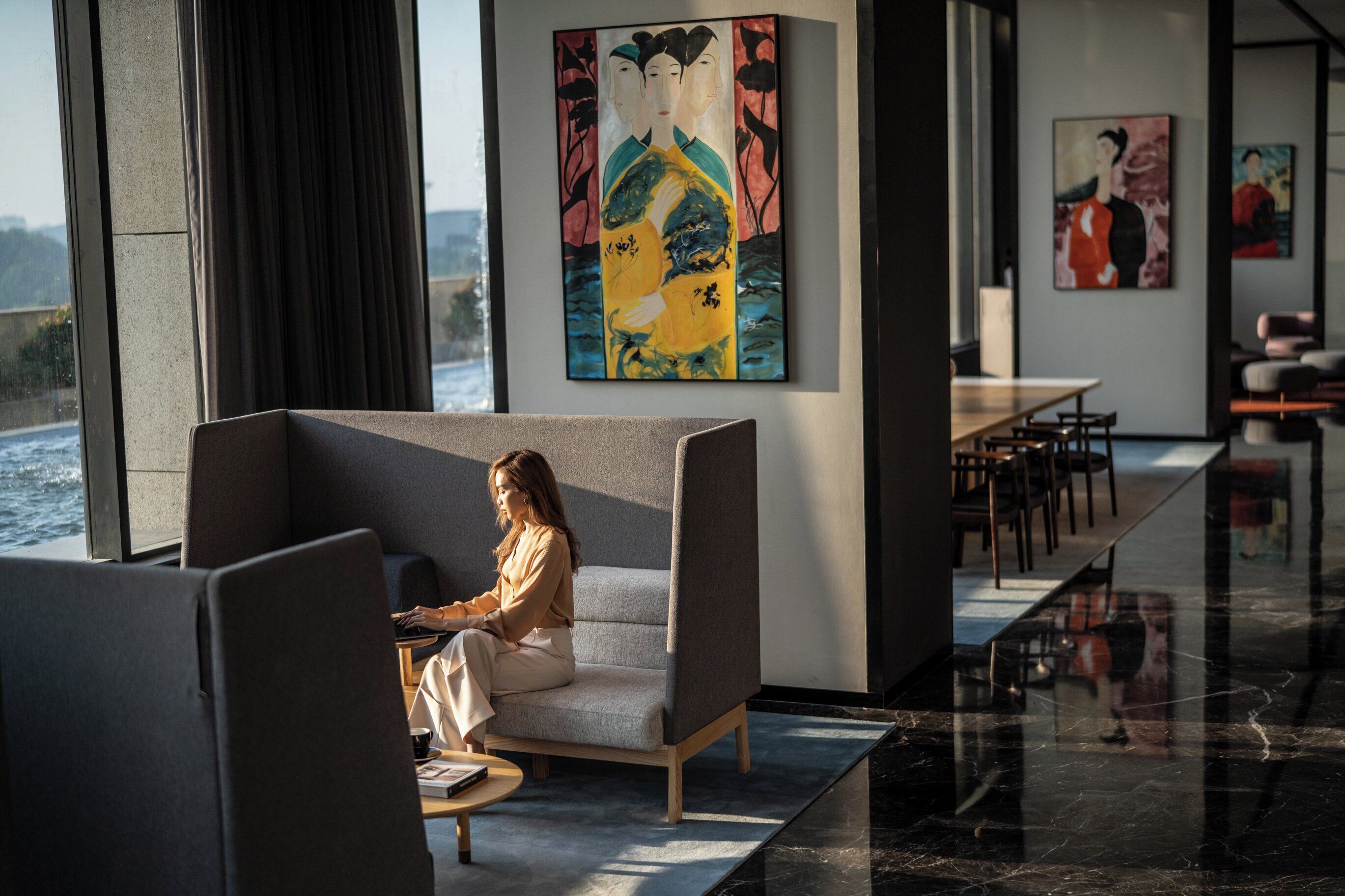 Un intérieur moderne comprenant un coin salon, une grande fenêtre donnant sur un plan d’eau et des œuvres d’art accrochées aux murs.