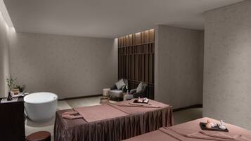 Un moderno spa con una bañera grande, dos camillas de masaje, una zona de estar con una silla y una mesita, y una pared con estanterías empotradas.