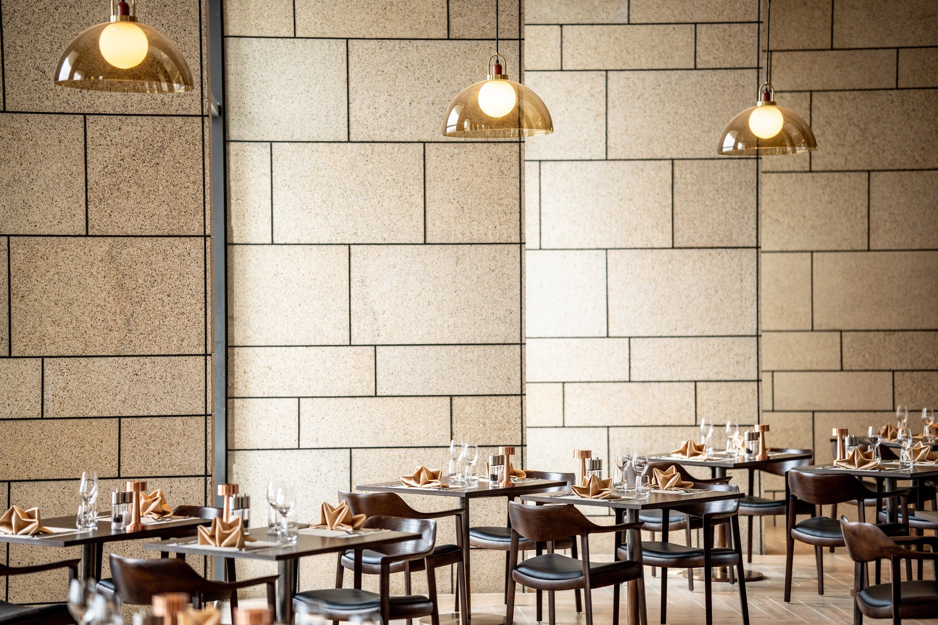 A restaurant with multiple tables, chairs, and hanging pendant lights.