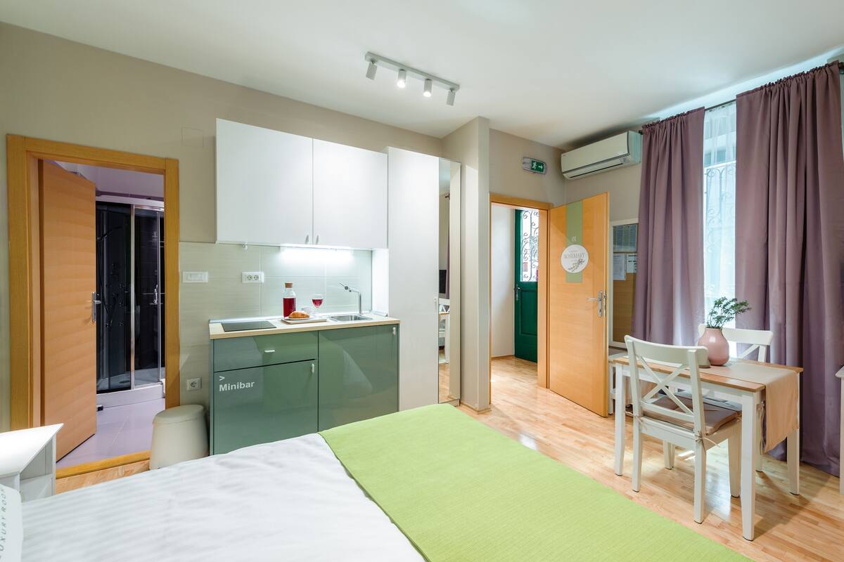 Ein Hotelzimmer mit Bett, Schreibtisch, Stuhl, Fernseher und einer Küchenzeile.