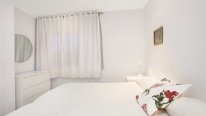 Een slaapkamer met een bed, nachtkastje, lamp, spiegel en een raam met gordijnen.
