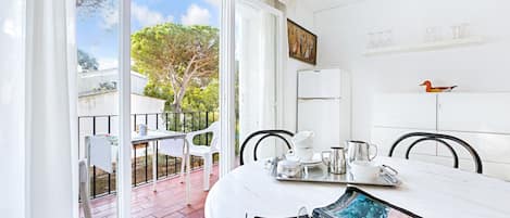 A bright, sunlit room with a dining table set for two, featuring a tray with teaware and a magazine.