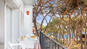 A balcony with a table set for dining, overlooking a beach and trees.