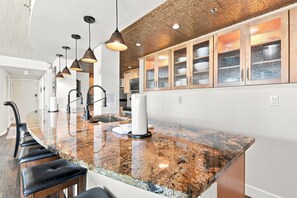Cocina con encimera de granito, iluminación colgante y muebles de madera.