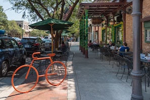 Eine Straße mit Außenbestuhlung eines Restaurants, einem Fahrrad und parkenden Autos.