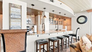 A modern kitchen with a central island, bar stools, and a wall-mounted clock.