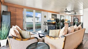 A spacious living area with a sofa set, a round glass table, and a ceiling fan.