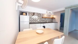 Una cucina moderna con forno a microonde, frigorifero e lavatrice. È presente un tavolo di legno con sedie e una ciotola.