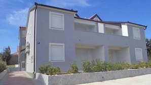 A two-story residential building with a grey facade, white windows, and a red brick pathway leading to the entrance. - Apartment Ugljanski Gusari (Preko)