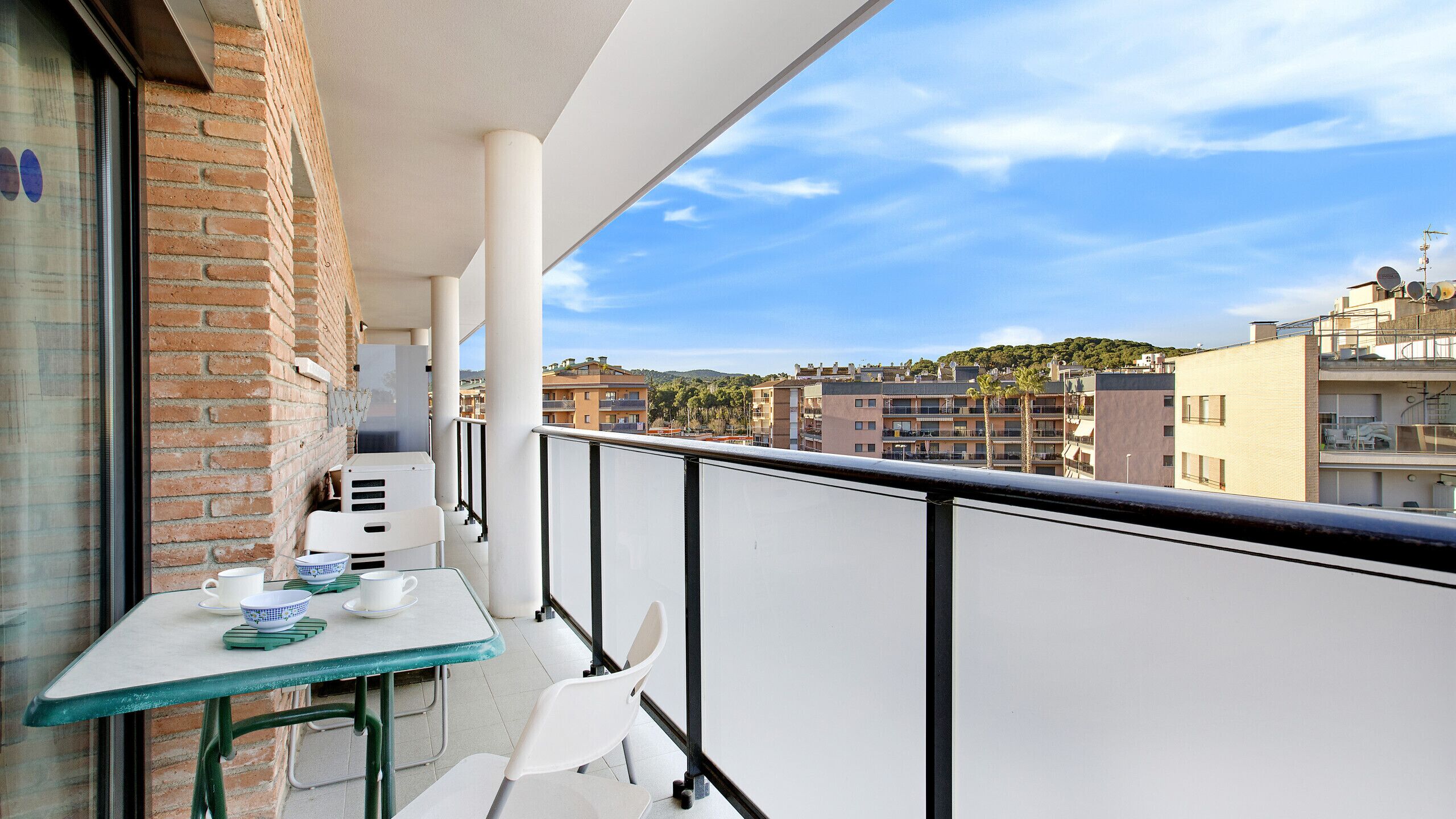 Een balkon met een tafel, stoelen en uitzicht op de stad.