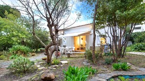 A house with a patio area, surrounded by a garden with various plants and a small pond.