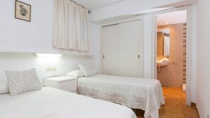 A hotel room with two beds, a white wardrobe, a bathroom visible through an open door, and a wall-mounted picture.