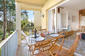 A wooden dining table set with plates, glasses, and cutlery on a balcony with a view of trees and a building. - 1CEN A1 -Basic  apartment with communal garden and pool, only 800m from the  beach of Llafranc (Llafranc)
