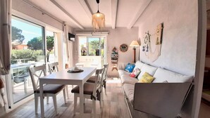 A cozy interior with a dining area, a sofa with colorful cushions, and a bar area visible through a glass door. - 1CB K2 -2 Bedroom apartment in a very quiet area with garden and communal pool near the beach of Calella de Palafrugell (Calella de Palafrugell)