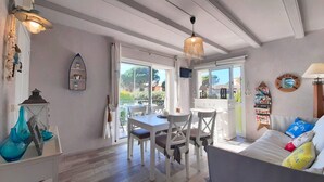 A cozy living room with a dining area, a sofa with colorful cushions, and a view of the outdoors. - 1CB K2 -2 Bedroom apartment in a very quiet area with garden and communal pool near the beach of Calella de Palafrugell (Calella de Palafrugell)