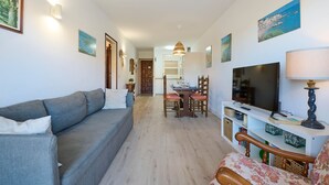 A living room with a sofa, a TV, a dining table with chairs, and a lamp.